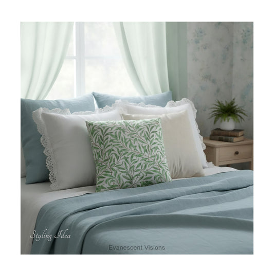 A square decorative cushion with green botanical pattern titled 'Willow Bough' by William Morris, shown styled on a bed with white and blue linens.