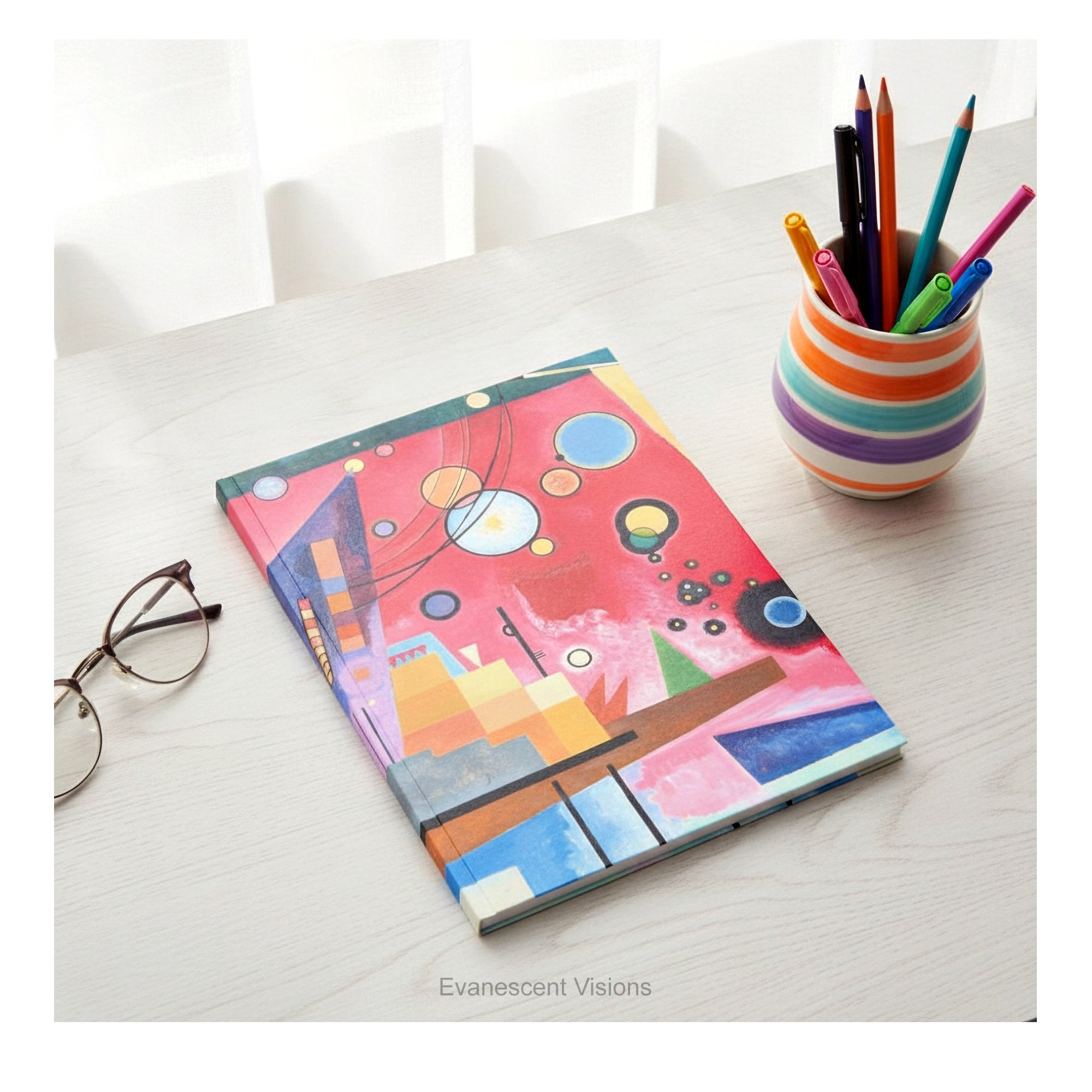 A hardcover notebook with a cover featuring  a colorful abstract geometric design titled 'Schweres Rot' by Kandinsky, shown on a desk with desk clutter.