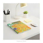 A hardback notebook featuring the colourful impressionistic floral artwork 'Bauerngarten' by Gustav Klimt, shown lying on a white desk with desk accessories.