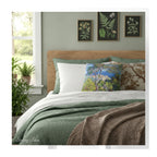 A square throw pillow printed with with Monet's Bordighera painting,  on a bed in a bedroom with botanical decor. 
