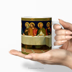 Hands holding a ceramic mug featuring religious painting 'The Last Supper' by Henry Siddons Mowbray. 