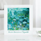 A white greeting card standing on a white surface, featuring Claude Monet's impressionist Water Lilies Painting in blue, green, and teal tones with the text 'Happy Birthday Elizabeth' below the artwork. 