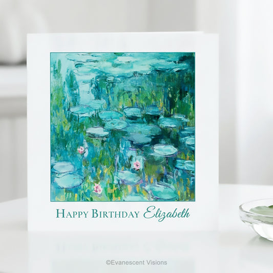A white greeting card standing on a white surface, featuring Claude Monet's impressionist Water Lilies Painting in blue, green, and teal tones with the text 'Happy Birthday Elizabeth' below the artwork. 