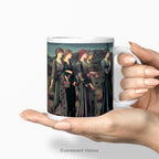 A hand holding a white ceramic mug featuring a print of Burne-Jones painting 'Psyche's Wedding. Wedding'  