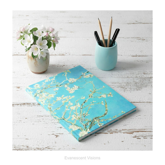 A hardback notebook with the floral impressionistic painting 'Almond Blossom' by Van Gogh, shown on a distressed white wood desk. 