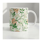 A ceramic mug featuring botanical pattern  'Jasmin'  by William Morris on a table.
